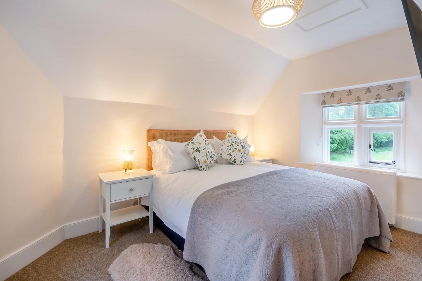 A bedroom with a bed, nightstands, a window with a view, and a ceiling light fixture.