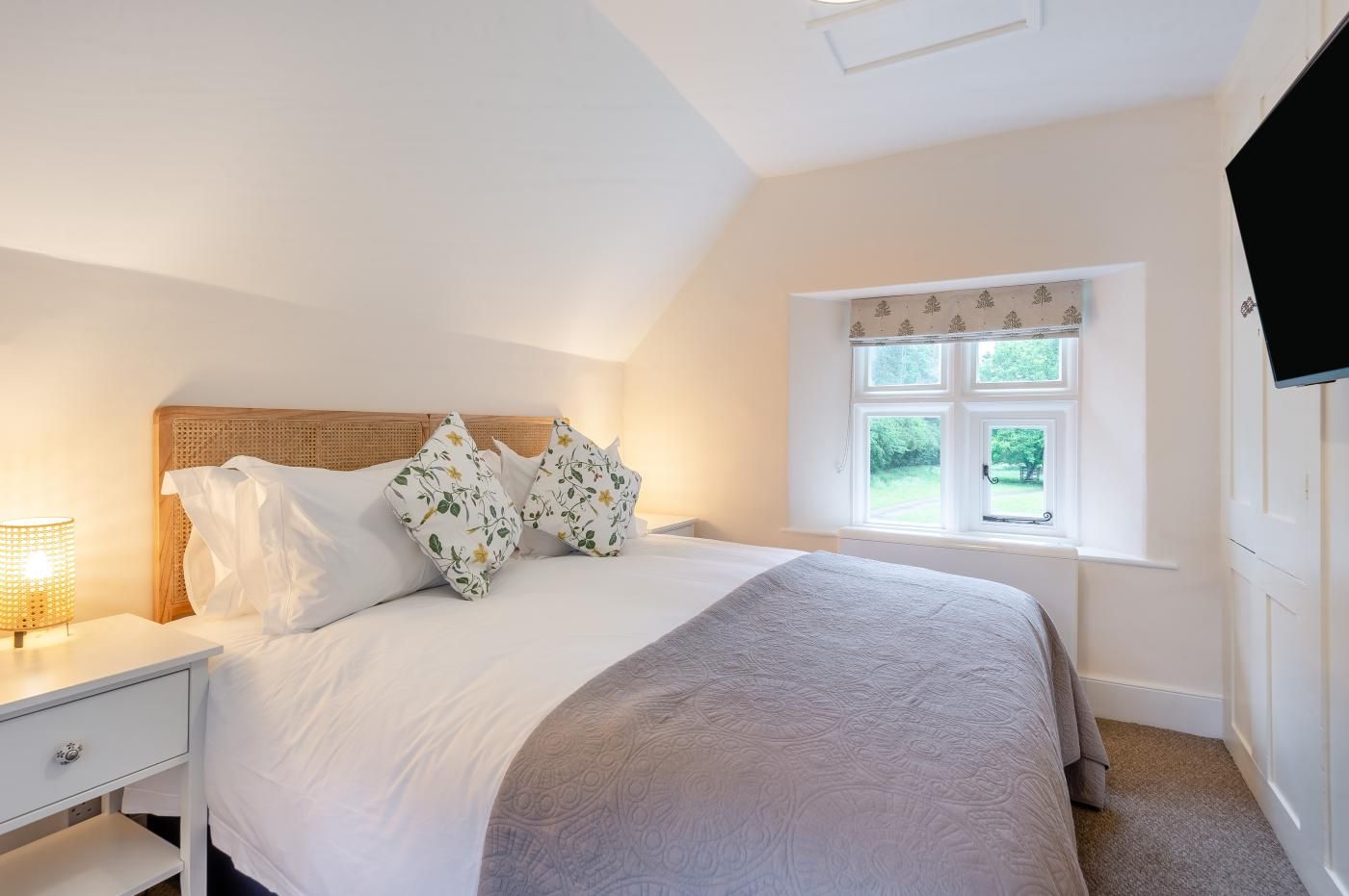 A bedroom with a bed, a nightstand, a window with a view, and a television.