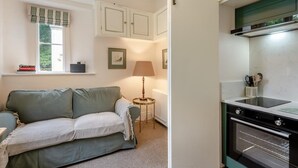 A compact living space with a sofa, a small table with a lamp, a window with curtains, and a kitchenette with a stove. - 1 Bed in Exton (oc-e42799) (Exton)