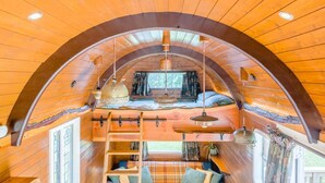 A cozy cabin with a loft bedroom, wooden walls, and a curved ceiling.