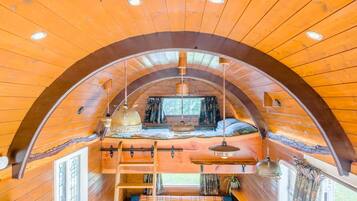 A cozy cabin with a loft bedroom, wooden walls, and a curved ceiling.
