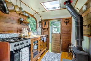 A compact kitchen with a gas stove, wooden cabinets, and a black chimney.
