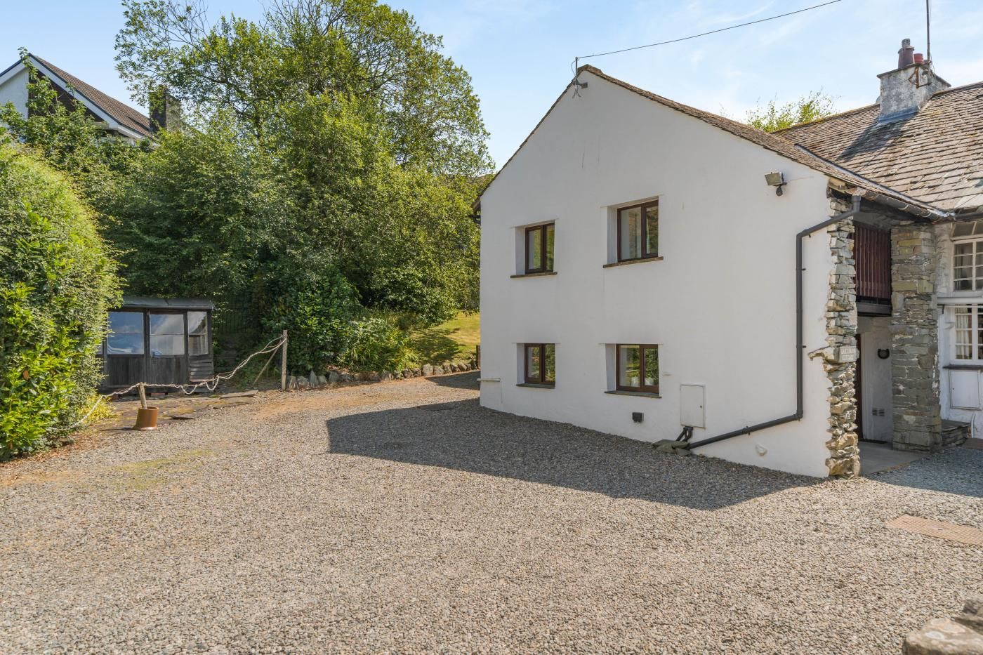 A white building with a gravel driveway, a small wooden structure, and a stone wall.