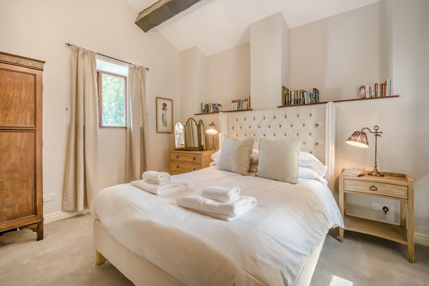 Een slaapkamer met een groot bed, een houten garderobe, een nachtkastje met een lamp en een boekenplank.
