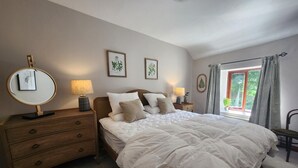 Ein Schlafzimmer mit einem großen Bett, Nachttischlampen, einem Schminktisch und gerahmten Pflanzenbildern an der Wand.