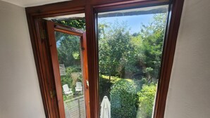 Eine Glastür führt in einen Garten mit einer Holzterrasse und weißen Stühlen.