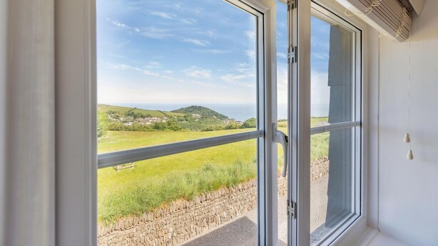 Habitació amb un gran finestral corredís que dona a un balcó amb vistes a un paisatge verd i turons.
