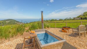 Ofurô com vista para o mar, rodeado por um deck de madeira e mobiliário externo.