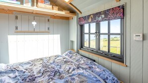 Um quarto com cama, janela com vista, estante com objetos e termostato.
