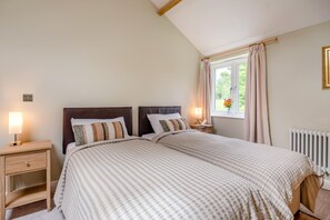 A double bed with a patterned bedspread, two bedside tables with lamps, a window with curtains, and a radiator. - 2 Bed in Laxton (oc-p44858) (Laxton)