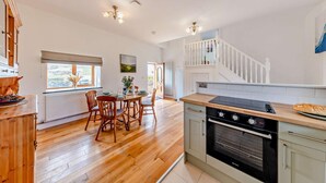 Una cocina con piso de madera, un comedor con sillas, una escalera y vistas al exterior.