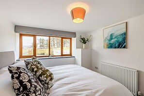 A bedroom with a large bed, a window with a view of trees, a radiator, and a painting on the wall. - 4 Bed in Rhoslefain (oc-br8) (Rhoslefain)