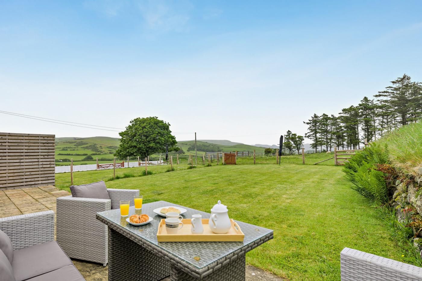 A patio with outdoor furniture, a table set with breakfast items, and a view of a grassy field and trees.