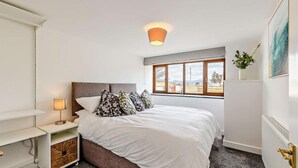 Un dormitorio con cama, mesita de noche, lámpara, ventana con vistas y radiador.