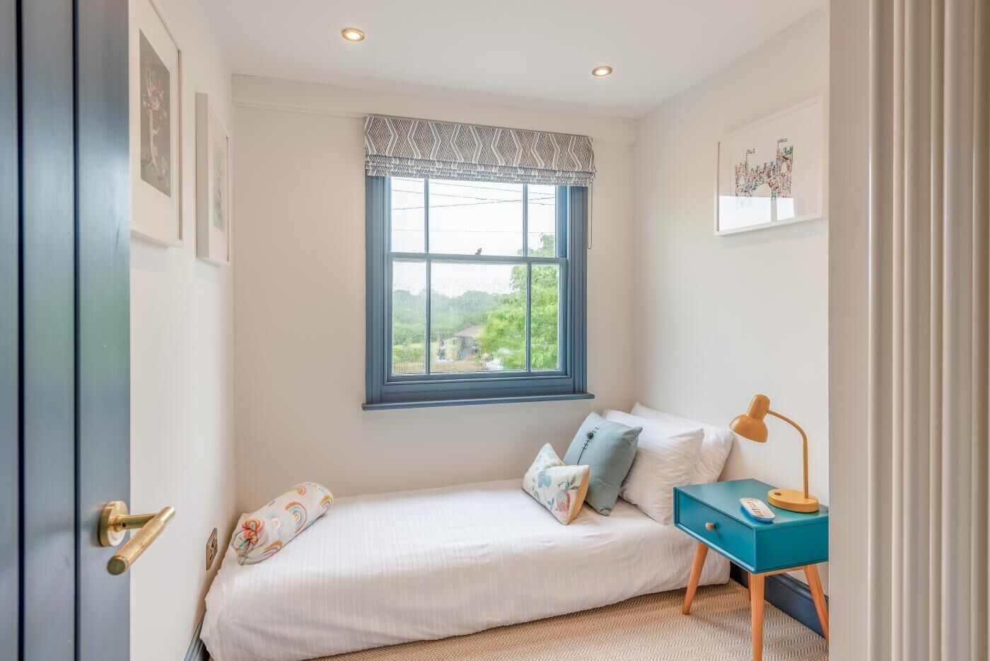 A bedroom with a bed, a window with a view, a bedside table with a lamp, and a door.