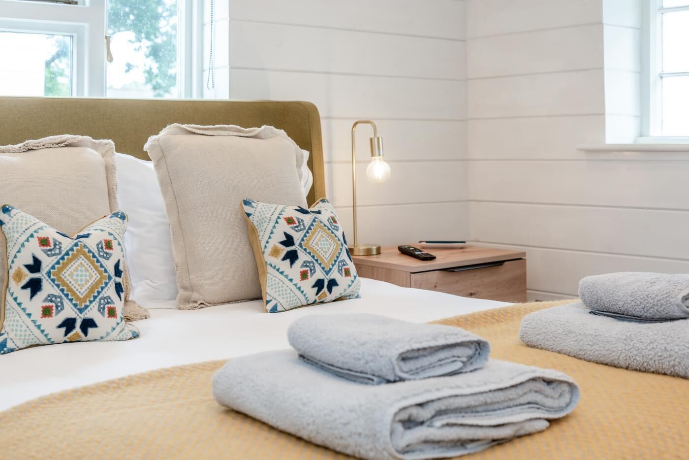 A neatly made bed with pillows, a bedside lamp, and folded towels.