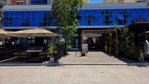 Un edificio moderno con fachada de vidrio, zona de estar al aire libre con sombrillas y una pequeña entrada.