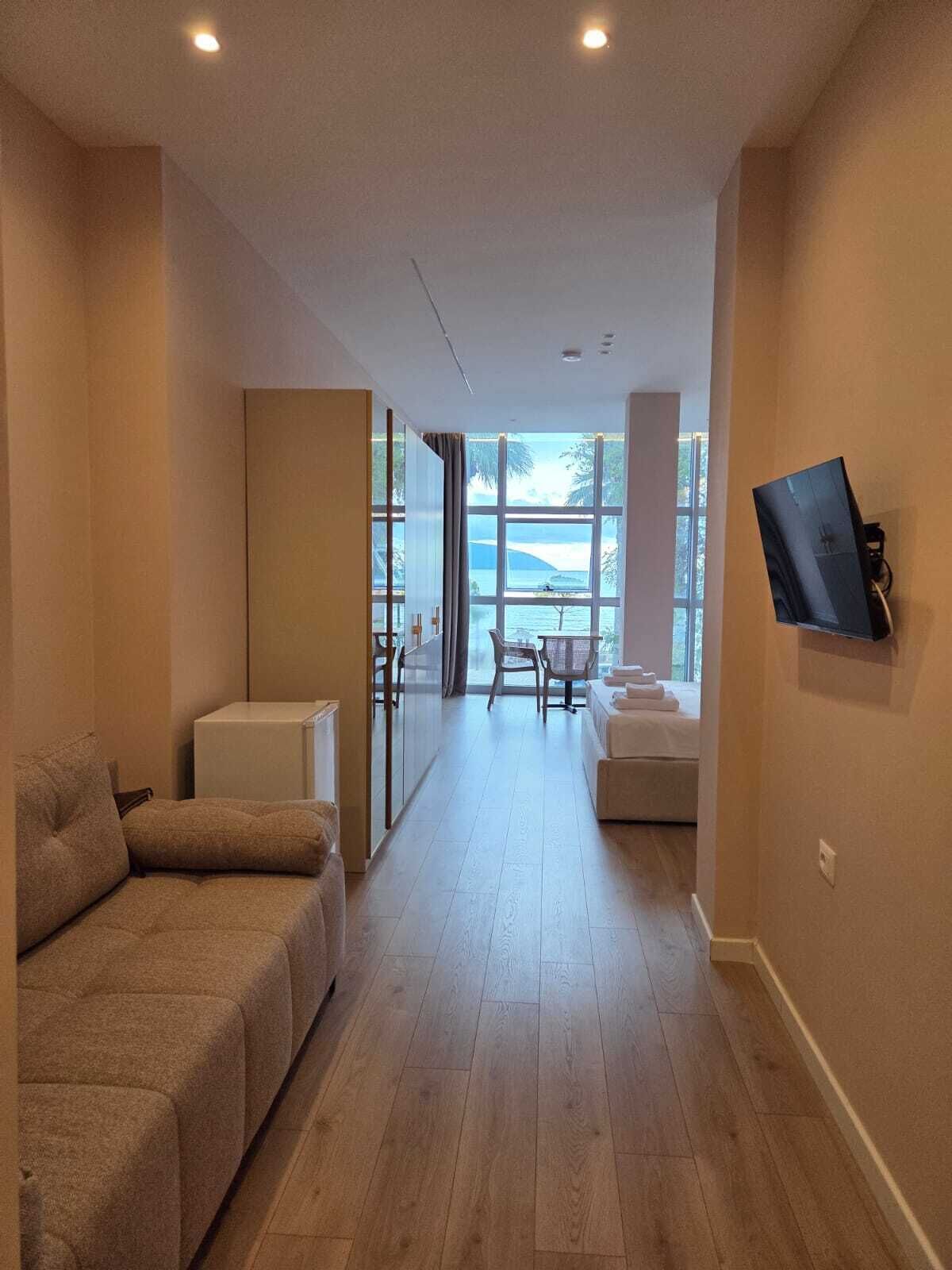Habitación de hotel con sofá, una mesita, televisor montado en la pared y vista al mar a través de amplias ventanas.