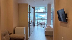 Habitación de hotel con sofá, una mesita, televisor montado en la pared y vista al mar a través de amplias ventanas.