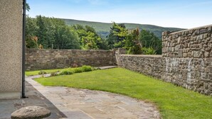 A stone wall, a stone patio, and a grassy area with a view of hills. - 2 Bed in Gilwern (oc-w44859) (Gilwern)