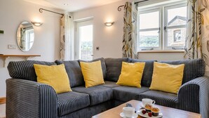 A modern living room with a sectional sofa, a wooden coffee table, and a view of a stone building through the windows. - 2 Bed in Gilwern (oc-w44859) (Gilwern)
