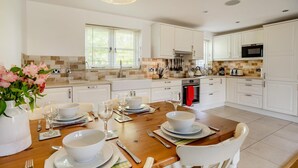 A modern kitchen with white cabinets, a dining table set for four, and a large window with blinds. - 2 Bed in Gilwern (oc-w44859) (Gilwern)