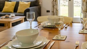 A dining table set with plates, bowls, and wine glasses, with a sofa and a window in the background. - 2 Bed in Gilwern (oc-w44859) (Gilwern)