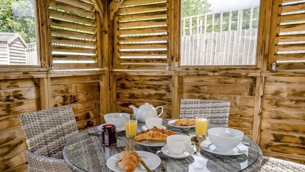 A breakfast table set with croissants, juice, and coffee in a wooden cabin with wicker chairs. - 2 Bed in Gilwern (oc-w44859) (Gilwern)
