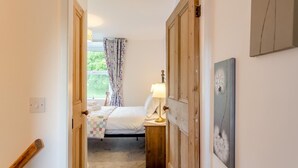 Un dormitorio con cama, lámpara de noche, ventana con cortinas y puerta que da a otra habitación.