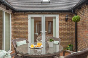 A glass-top table with wicker chairs, a breakfast setting, and a brick wall. - 2 Bed in Buxted (oc-t44744) (Buxted)