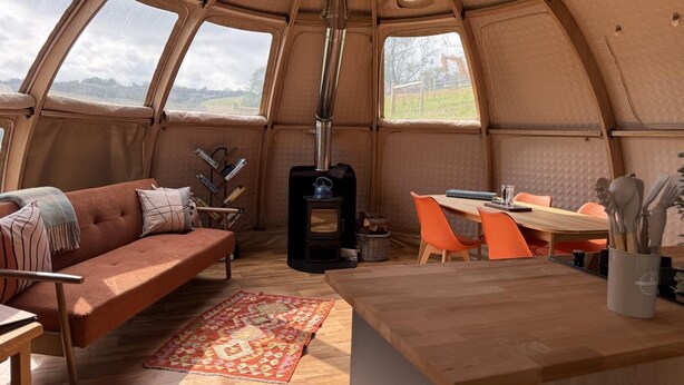 A cozy interior with a sofa, a table, chairs, a rug, and a wood-burning stove.
