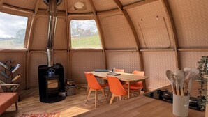 A cozy interior with a wood-burning stove, a dining table with chairs, and a view of the outdoors.