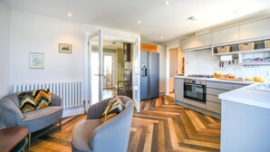 Una cocina moderna con refrigerador, horno y lavamanos. Hay dos sillas con cojines y un radiador en la pared.