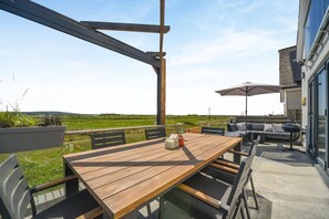 Eine Außenpatio mit einem Holztisch und Stühlen, einem Grill und einer Couch mit Sonnenschirm.