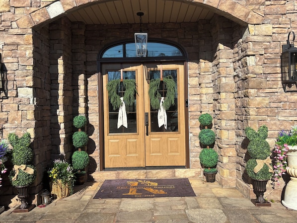 A stone building with a wooden double door, a doormat, and potted plants.