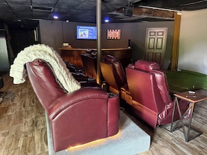 A room with leather reclining chairs, a massage chair, a reception desk, and a screen displaying information.