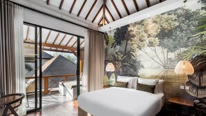 A bedroom with a large bed, a view of a house through glass doors, a mural of a forest, and a hanging light fixture. - Villa Nusantara 4 in Pererenan (Pererenan)