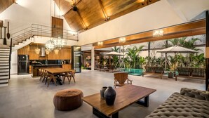 A spacious living area with a wooden dining table, a sofa, and a poolside seating area with umbrellas. - Villa Nusantara 4 in Pererenan (Pererenan)