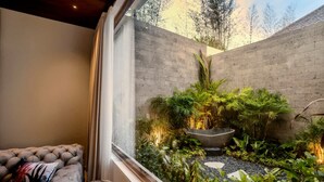 A modern interior with a cushioned seating area, a concrete wall, and a small indoor garden with various plants and a large pot. - Villa Nusantara 4 in Pererenan (Pererenan)