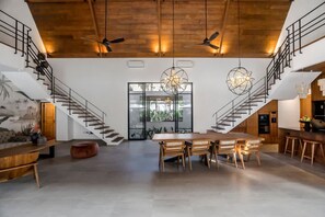 Un vaste espace de vie doté d’un haut plafond, d’un escalier en bois et d’une table à manger avec des chaises.