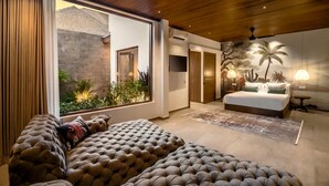 A modern bedroom with a large bed, a sofa, and a view of a garden through a sliding door. - Villa Nusantara 4 in Pererenan (Pererenan)