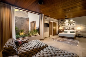 Ein modernes Schlafzimmer mit einem großen Bett, einer Couch und Blick auf einen Garten durch eine Schiebetür.