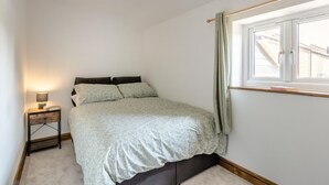 Een slaapkamer met een bed, een nachtkastje met lamp, een raam met gordijnen en uitzicht op een gebouw.