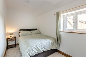Ein Schlafzimmer mit einem Bett, einem Nachttisch mit Lampe, einem Fenster mit Vorhängen und Blick auf ein Gebäude.