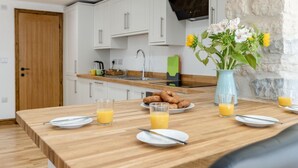 Een moderne keuken met witte kasten, een houten aanrecht en een ontbijt gedekte eettafel, met borden, sinaasappelsap en een bloevas.