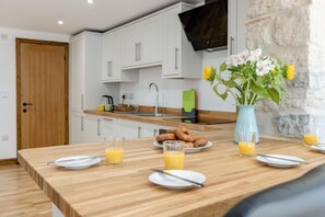 Eine moderne Küche mit weißen Schränken, einer Holz Arbeitsplatte und einem Esstisch, gedeckt für das Frühstück mit Tellern, Orangensaftgläsern und einer Blumenvase.