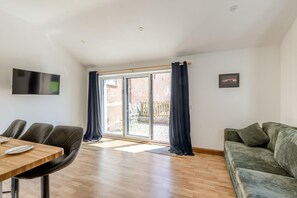 Ein geräumiges Wohnzimmer mit Holzboden, einer Couch, einem Esstisch mit Stühlen und einer Schiebetür zu einem Außenbereich.
