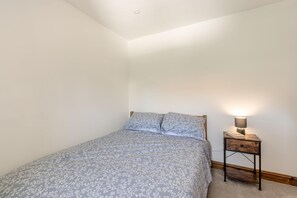Ein kleines Schlafzimmer mit einem Einzelbett, einem Nachttisch mit Lampe und einer schlichten weißen Wand.