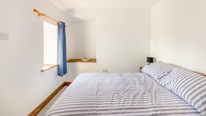 Une chambre à coucher avec un lit, une fenêtre avec des rideaux, une table de chevet et une étagère remplie de livres.