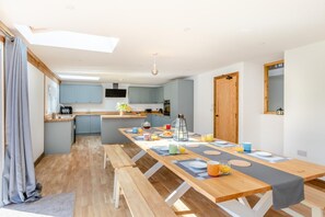 Eine moderne Küche mit hellblauen Schränken, einer zentralen Kochinsel und einem Essbereich mit einem langen Holztisch, gedeckt für das Frühstück.